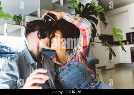 Romantic man kissing young woman holding VR headset in living room Stock Photo