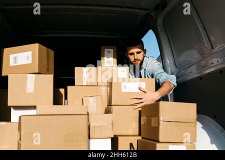 Man arranging brown boxes in van on sunny day Stock Photo