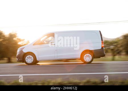 Delivery man driving van on road at sunset Stock Photo
