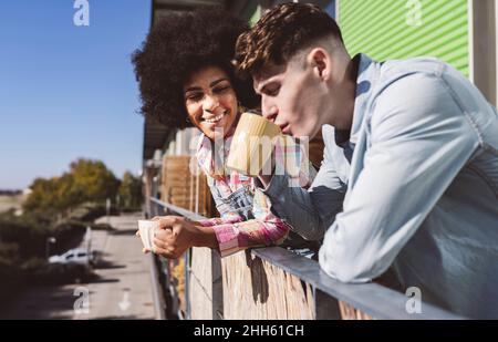 Young couple enjoying coffee together standing on balcony on sunny day Stock Photo