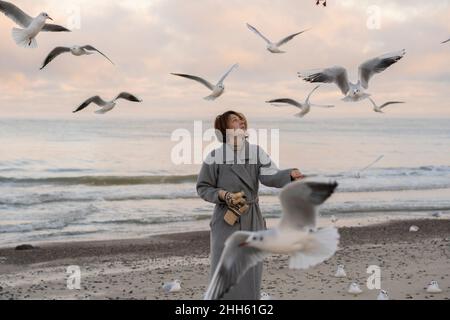 Young woman feeding seagulls on shore at beach Stock Photo