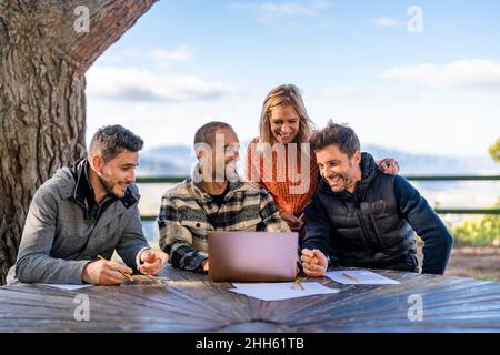 Cheerful man using laptop sitting with friends at table Stock Photo
