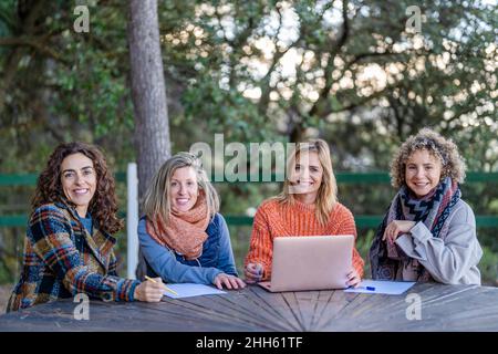 Happy female friends with laptop sitting at table in park Stock Photo