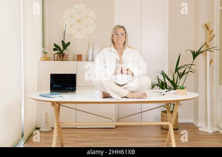 Businesswoman with hands clasped and eyes closed meditating on desk Stock Photo