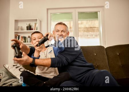 Grandfather and grandson enjoying playing video game at home Stock Photo