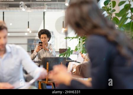 Businesswoman using mobile phone and colleagues discussing in office Stock Photo