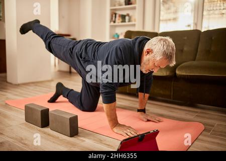 Senior man practicing yoga on exercise mat at home Stock Photo