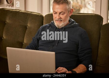 Smiling senior man using laptop sitting at home Stock Photo