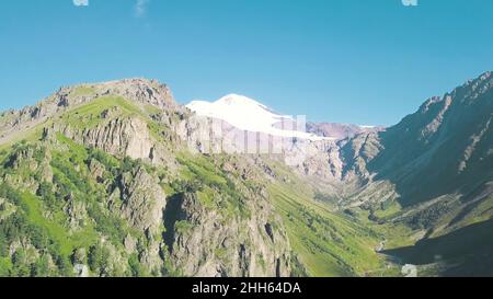 Top view of mountain landscape with snowy peak and green slopes. Clip. Majestic rocky mountains with green forest and snow-capped peaks. Spectacular m Stock Photo
