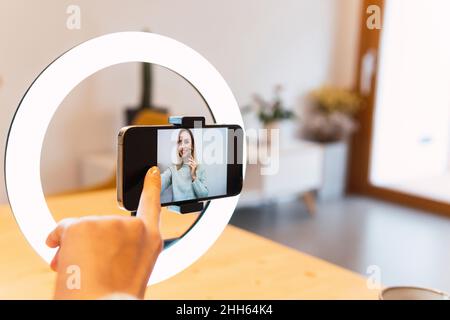 Influencer touching phone screen attached on ring light Stock Photo