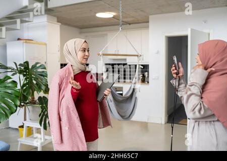 Woman photographing pregnant friend with file at home Stock Photo