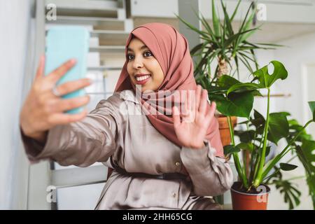Smiling woman waving on video call through smart phone at home Stock Photo