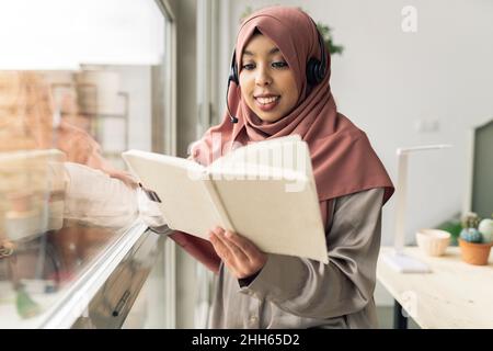 Smiling woman reading book in living room Stock Photo
