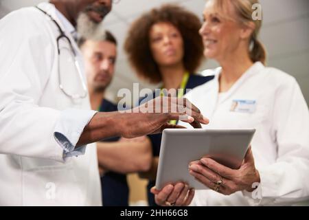 Doctor using tablet PC with colleagues in meeting at hospital Stock Photo