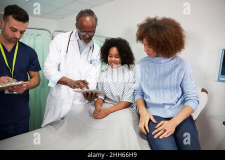 Patient with mother reviewing report over tablet PC held by doctor at hospital Stock Photo