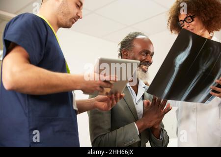 Smiling patient looking at X-ray with healthcare workers in medical room Stock Photo