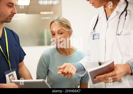 Senior patient looking at tablet PC by healthcare workers in medical room Stock Photo