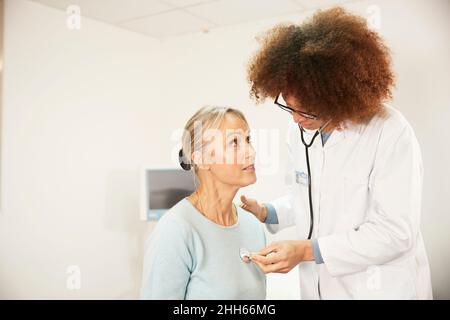 Doctor examining patient with stethoscope in medical room Stock Photo