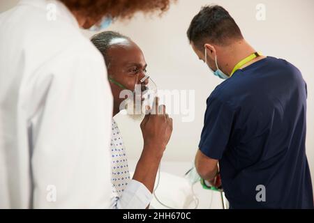 Patient wearing oxygen mask with healthcare workers in medical room Stock Photo