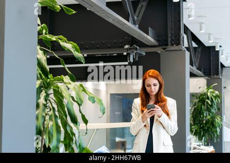 Working woman using mobile phone in corridor at workplace Stock Photo