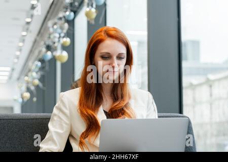 Redhead businesswoman using laptop in cafeteria at workplace Stock Photo