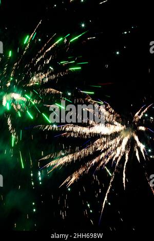 Green and yellow fireworks exploding against clear night sky Stock Photo