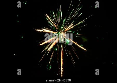 Green and yellow fireworks exploding against clear night sky Stock Photo