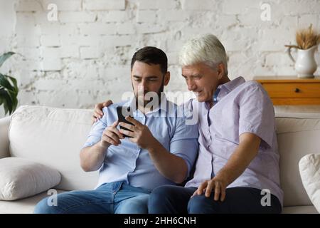 Focused grownup son teaching mature father to use online app Stock Photo