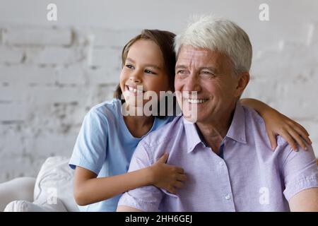 Thoughtful happy grandkid boy hugging dreamy mature grey haired grandfather Stock Photo