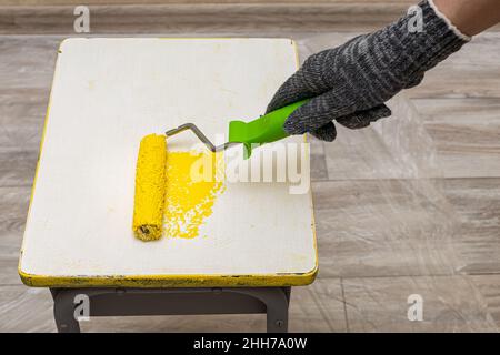 hand in motion paints a stool with yellow paint roller. High quality photo Stock Photo