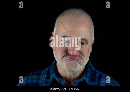 An old man makes a thoughtful grimace while looking down.   . Stock Photo