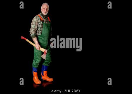 A woodcutter stands with his ax and cut-resistant boots in front of a black background. Stock Photo