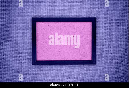 Mockup, abstract composition. Wooden frame on purple burlap. Inside the frame is a textured base in pink. Colors 2022 (very peri) Stock Photo