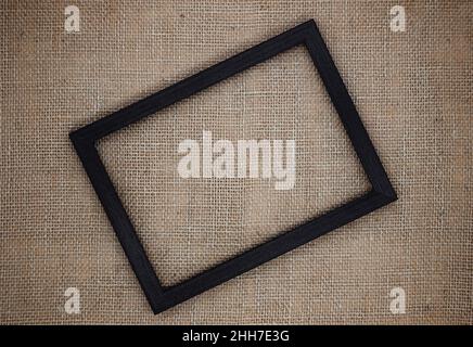 Abstract background. Mockup made from natural materials. Empty dark brown wooden frame on a background of burlap close-up. Stock Photo