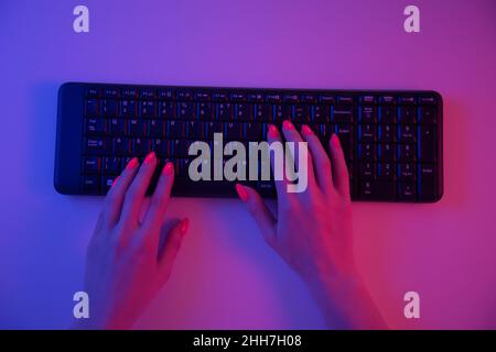 Woman working on wireless keyboard in neon light, pov. Stock Photo