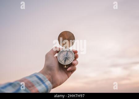 Vintage compass in the hands of the traveler against the sky during sunset. Stock Photo