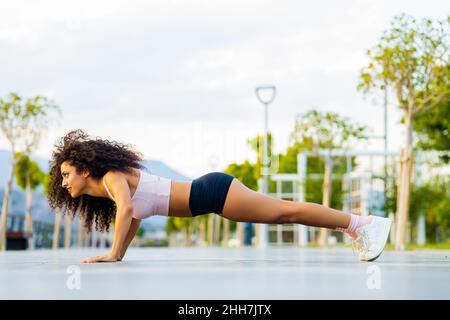 latin hispanic woman with afro curls doing push-ups in park outdoors Stock Photo