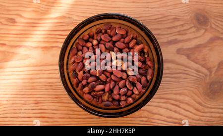 Fried peanuts in peel, peeled groundnuts in white glass plate on wooden background. Stock Photo