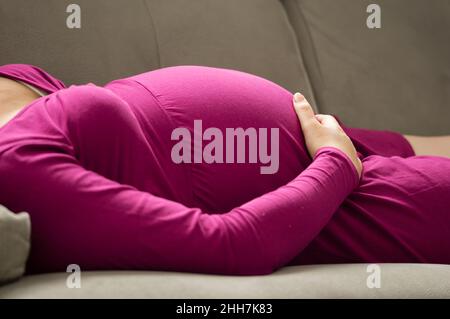 Close-up of a hand pregnant woman lying on sofa at home Stock Photo