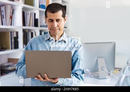 Cropped portrait of a handsome young businessman working on his laptop while standing in the office Stock Photo