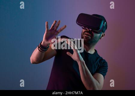 Young man in VR glasses excited interact with virtual reality in color neon light, future technology, education video gaming Stock Photo