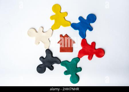 Brown plasticine house in the center of multi-colored bright plasticine men in a circle isolated on a white background, flat lay, top view. Family con Stock Photo