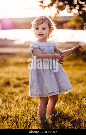 Cute, little girl in white dress looking at something. Afternoon light Stock Photo