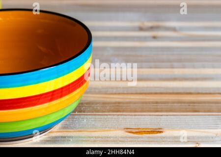 Close-up photo of a striped bowl, colored in red, blue, yellow, orange and green, on a wooden background; copy space Stock Photo