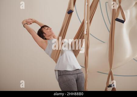 Mature woman enjoying stretching her back on aerial yoga hammock Stock Photo