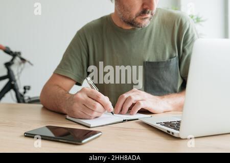 Telecommuter writing project notes in notebook at home office desk, selective focus Stock Photo