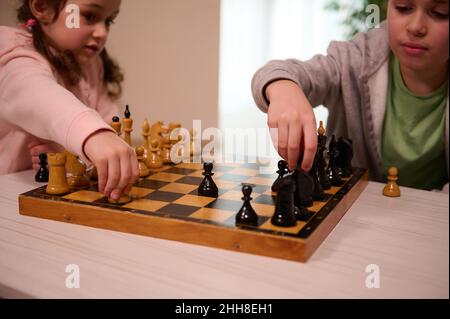 Soft focus on the hands of a happy boy and little girl playing chess in home interior. Smart intellectual board games for kids, logic development, edu Stock Photo