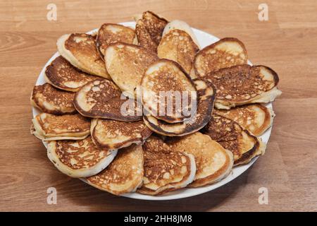 A lot of homemade small thick pancakes on white plate. Top view. Traditional russian sweet dessert. Mini pancakes on the table. Stock Photo