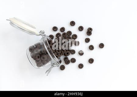 corn rings for breakfast, tasty black and cereal rings poured out of glass jar on white background, concept healthy food Stock Photo