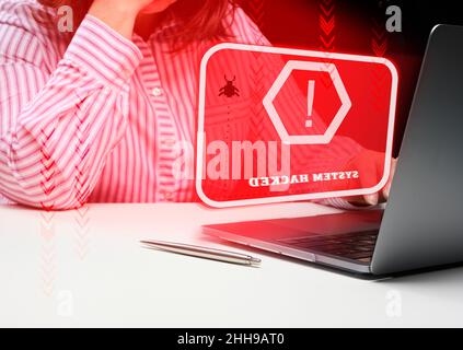 a woman sits at a laptop, in front of her is the inscription the system is hacked. User hacker attack, system hacking, password stolen Stock Photo